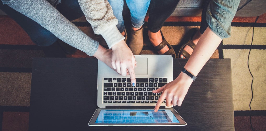 A group of students gathered around and gesturing at a laptop